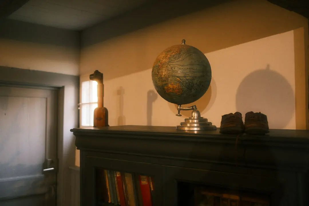 An old globe on a dark bookcase lit by warm afternoon light