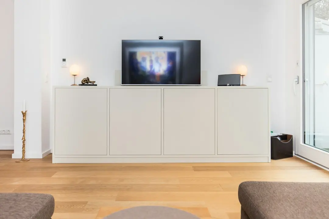 A wall-mounted TV above a white sideboard in a bright living room, with a small box beside it