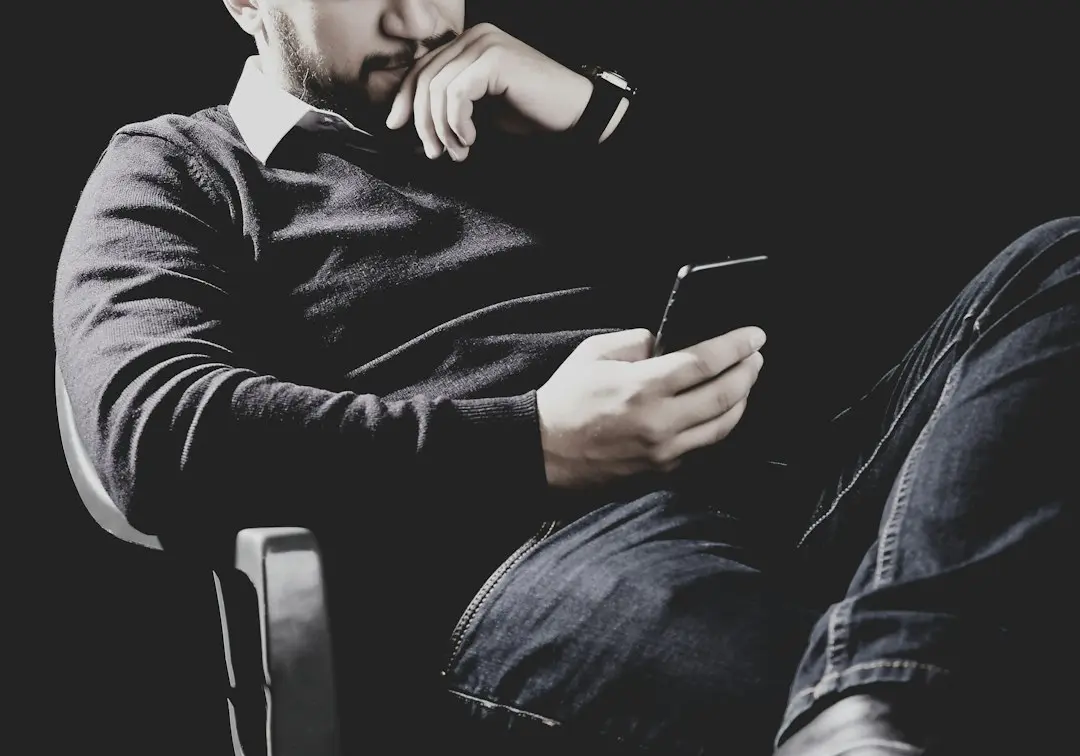 A man in a dark room holding a smartphone, ready to pick an IPTV player app